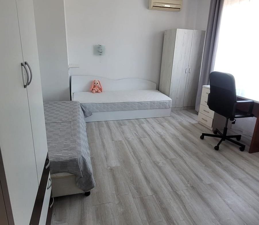 Современная спальня в Болгарии с односпальной кроватью, рабочим столом и шкафом, светлые тона и деревянный пол.