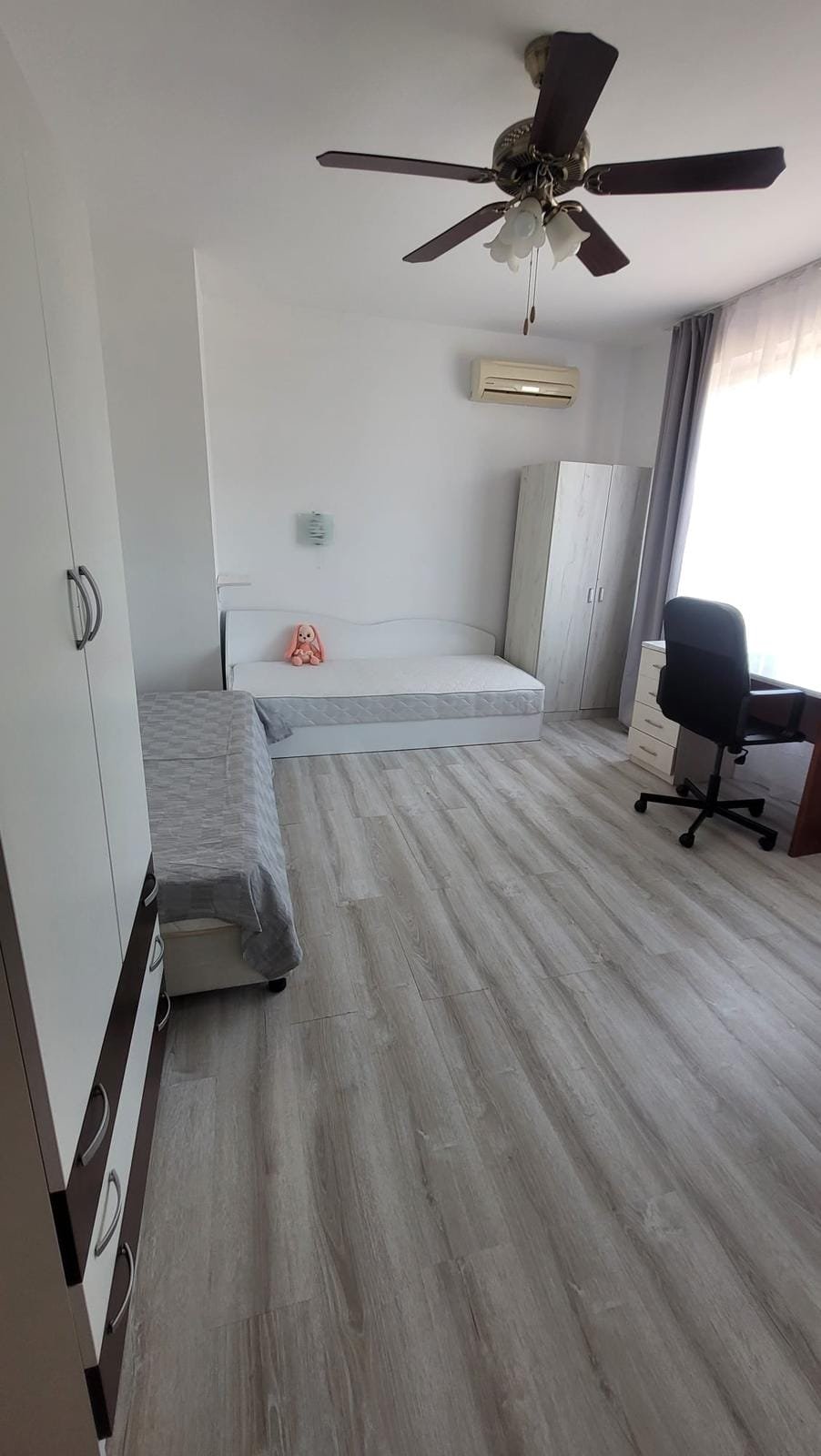 Современная спальня в Болгарии с односпальной кроватью, рабочим столом и шкафом, светлые тона и деревянный пол.