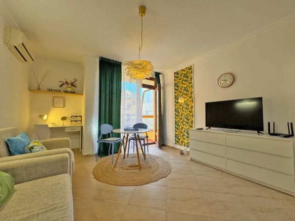 Современная гостиная с круглым столом, удобным диваном и телевизором, яркое оформление, в районе Святого Власа, идеальное жилье у моря.