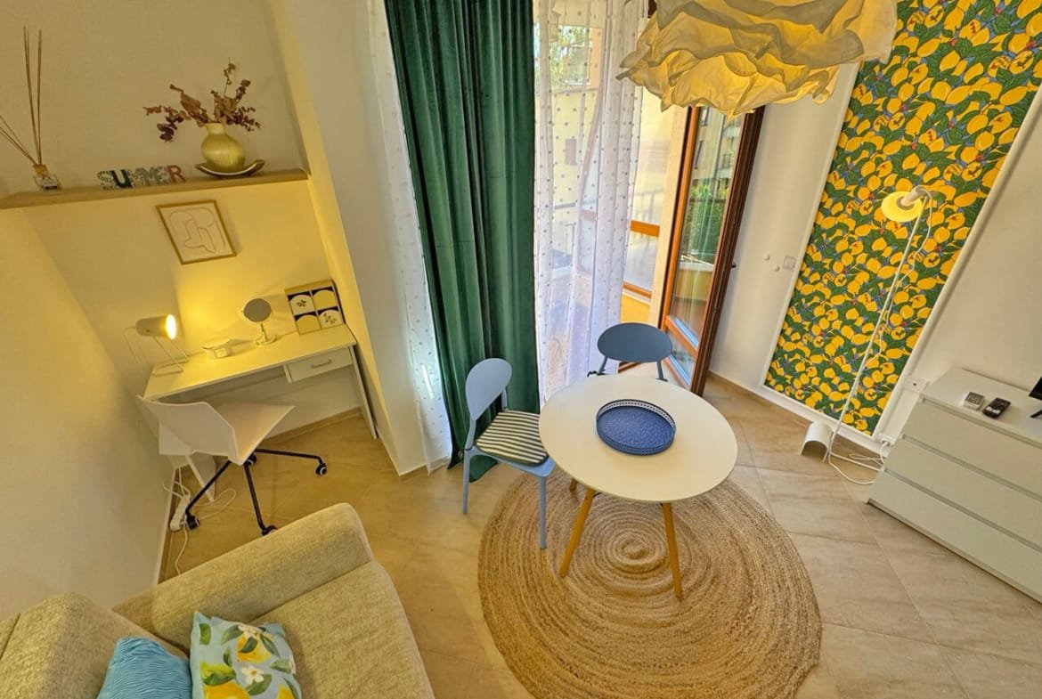 Современная гостиная с уютным интерьером, столом и стульями, светлым текстилем и яркой желтой акцентной стеной.