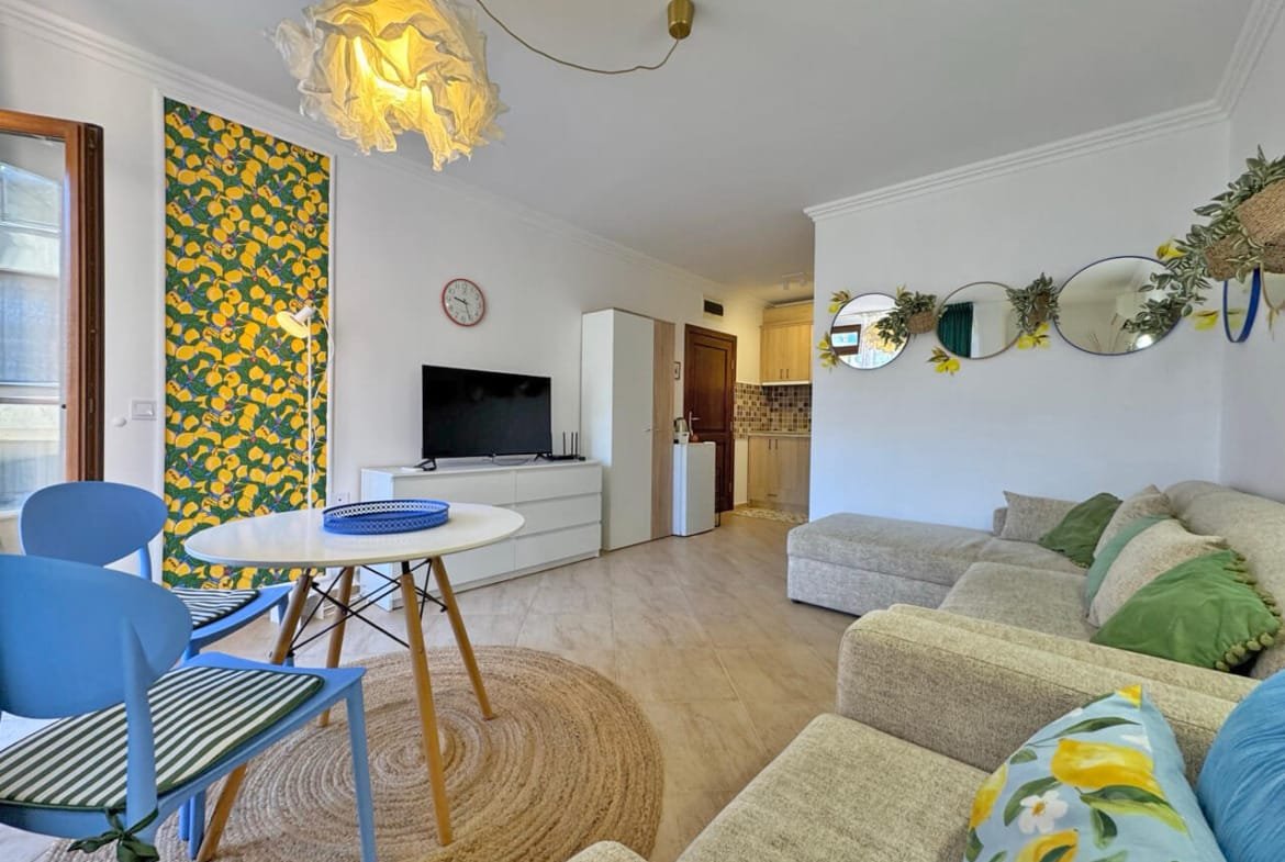 Современная гостиная с зеленым диваном, круглым столом и яркими акцентами, расположенная в квартире на курорте в Болгарии.