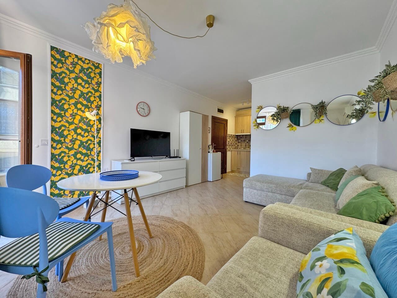 Современная гостиная с зеленым диваном, круглым столом и яркими акцентами, расположенная в квартире на курорте в Болгарии.