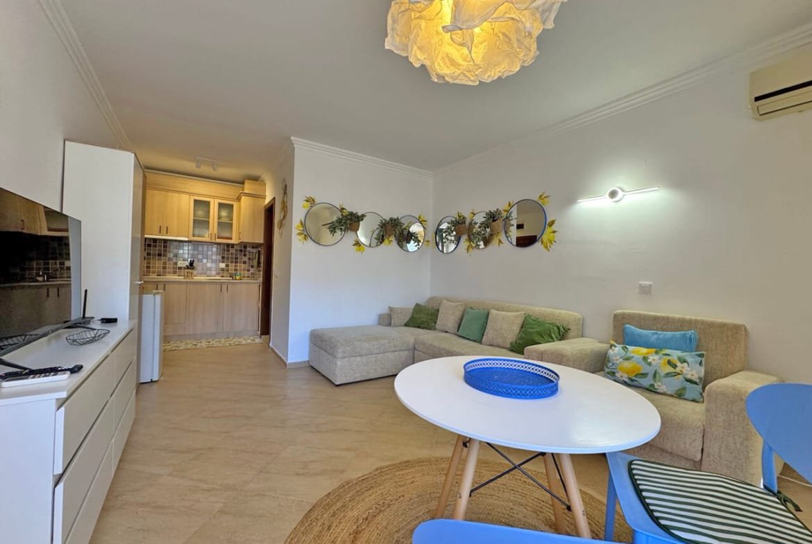 Современная гостиная с уютным диваном, яркими акцентами и кухонной зоной, идеально подходит для апартаментов в Болгарии.