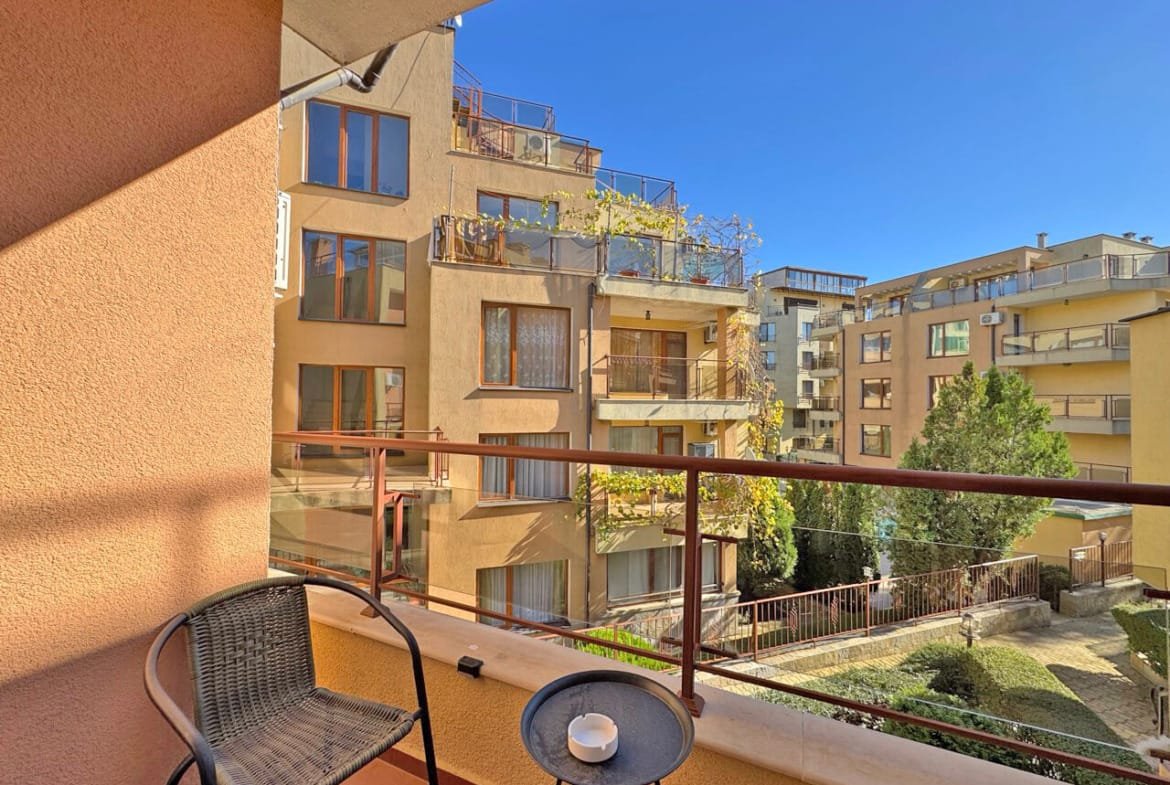 Уютная терраса с двумя креслами и столиком, вид на жилые корпуса, зелень и яркое солнечное небо в районе Солнечного берега.