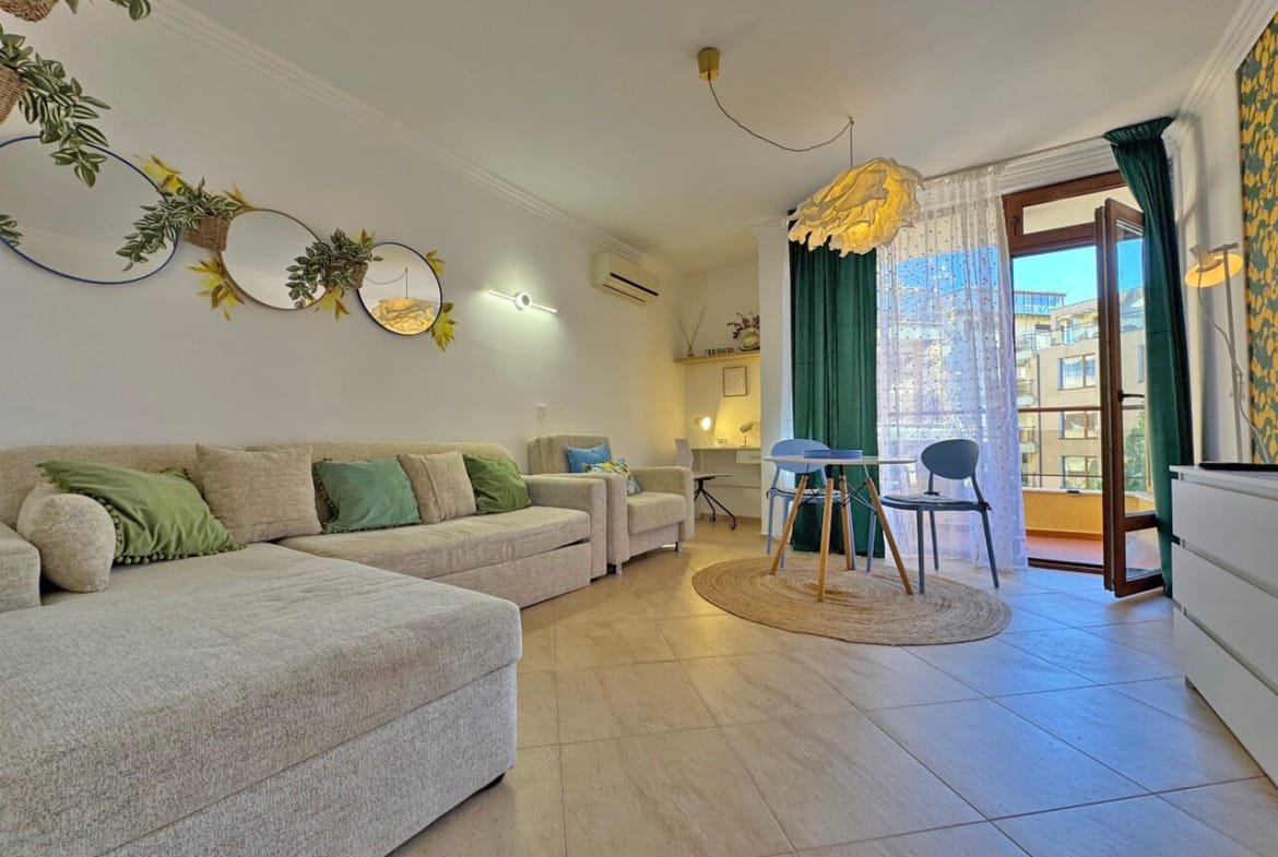 Современная гостиная с диваном, столом и зелеными шторами, выходящая на балкон. Идеальное жилье рядом с берегом в Болгарии.