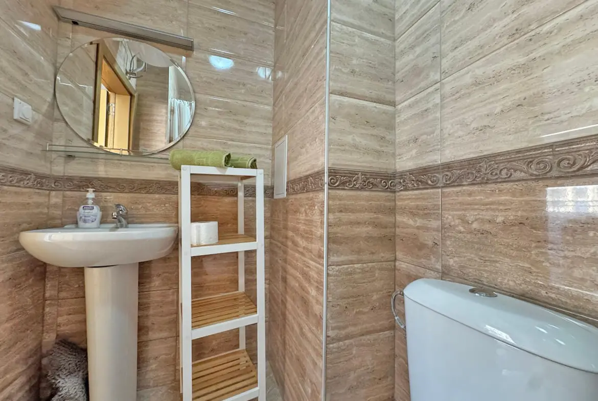 Современная ванная комната с умывальником, зеркалом, туалетом и открытыми полками, отделка в светлых тонах.