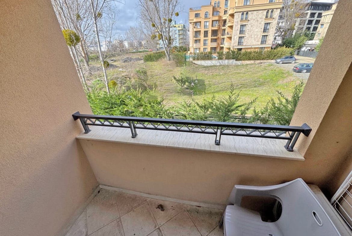 Балкон с видом на зелёный участок и жилые дома в Болгарии, идеальный для апартаментов у моря.