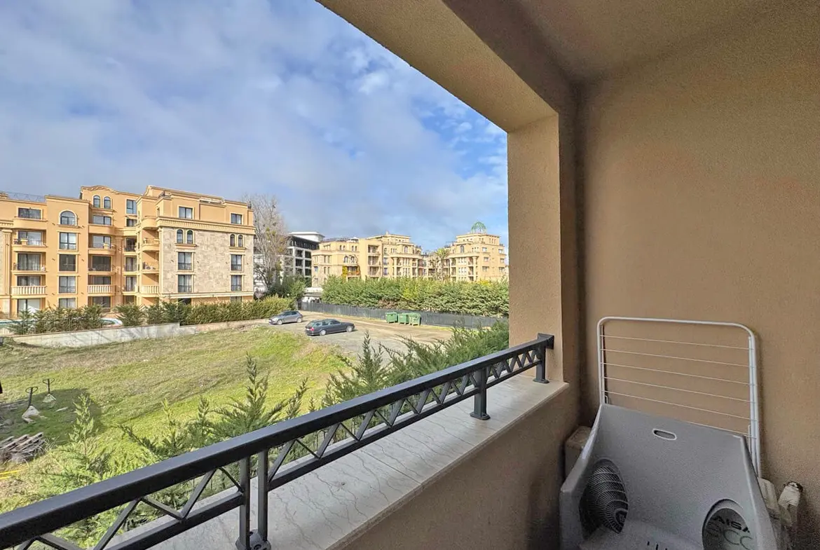 Балкон с видом на жилые комплексы в Болгарии, зелёные насаждения и парковка, идеальное место для апартаментов у моря.
