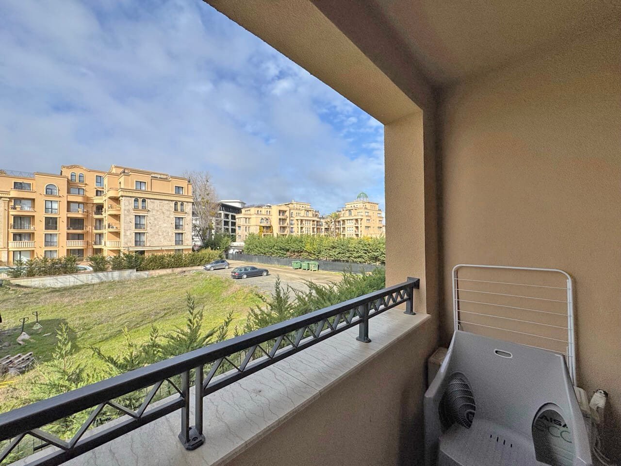 Вид с балкона на жилой комплекс и зеленую территорию. Балкон с видом на жилые комплексы в Болгарии, зелёные насаждения и парковка, идеальное место для апартаментов у моря.