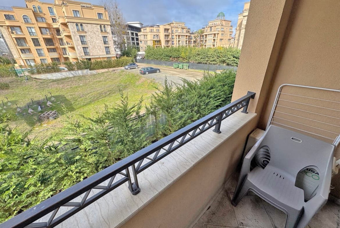 Балкон с пластиковым креслом, вид на зелёную территорию и жилые комплексы, идеальное жилье у моря.