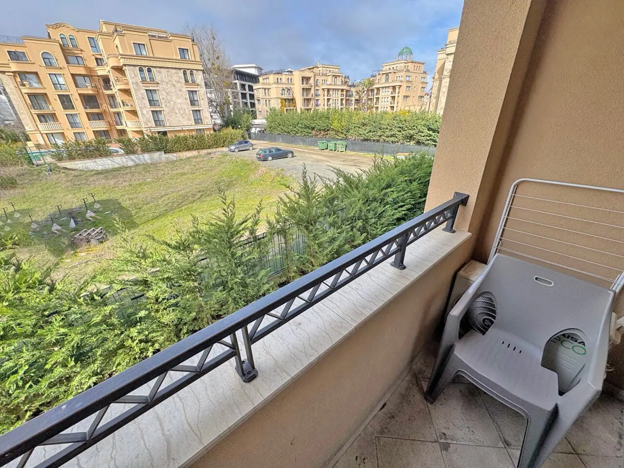 Балкон с пластиковым стулом и видом на жилые здания. Балкон с пластиковым креслом, вид на зелёную территорию и жилые комплексы, идеальное жилье у моря.