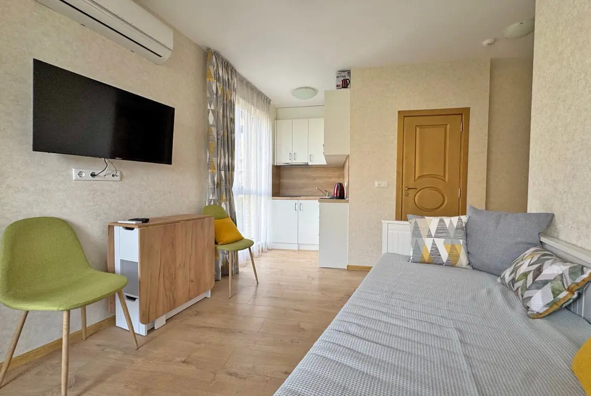 Современная квартира-студия с кухонной зоной, гостиной и видом на море, обставленная стильной мебелью.