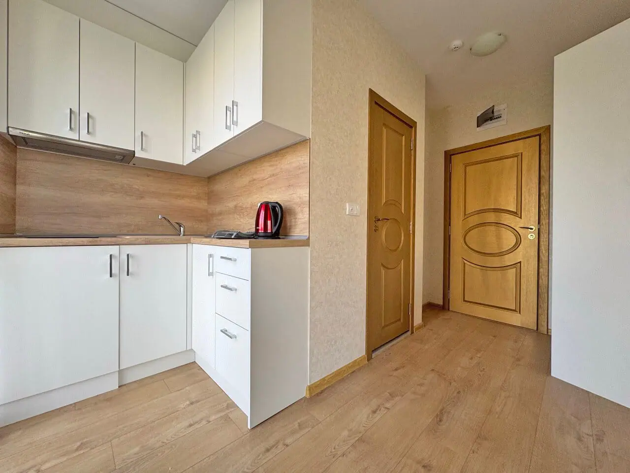 Современная кухня в квартире с дверью и полом из дерева Современная кухня в квартире, с деревянными полу и светлой мебелью, ждет новых владельцев.