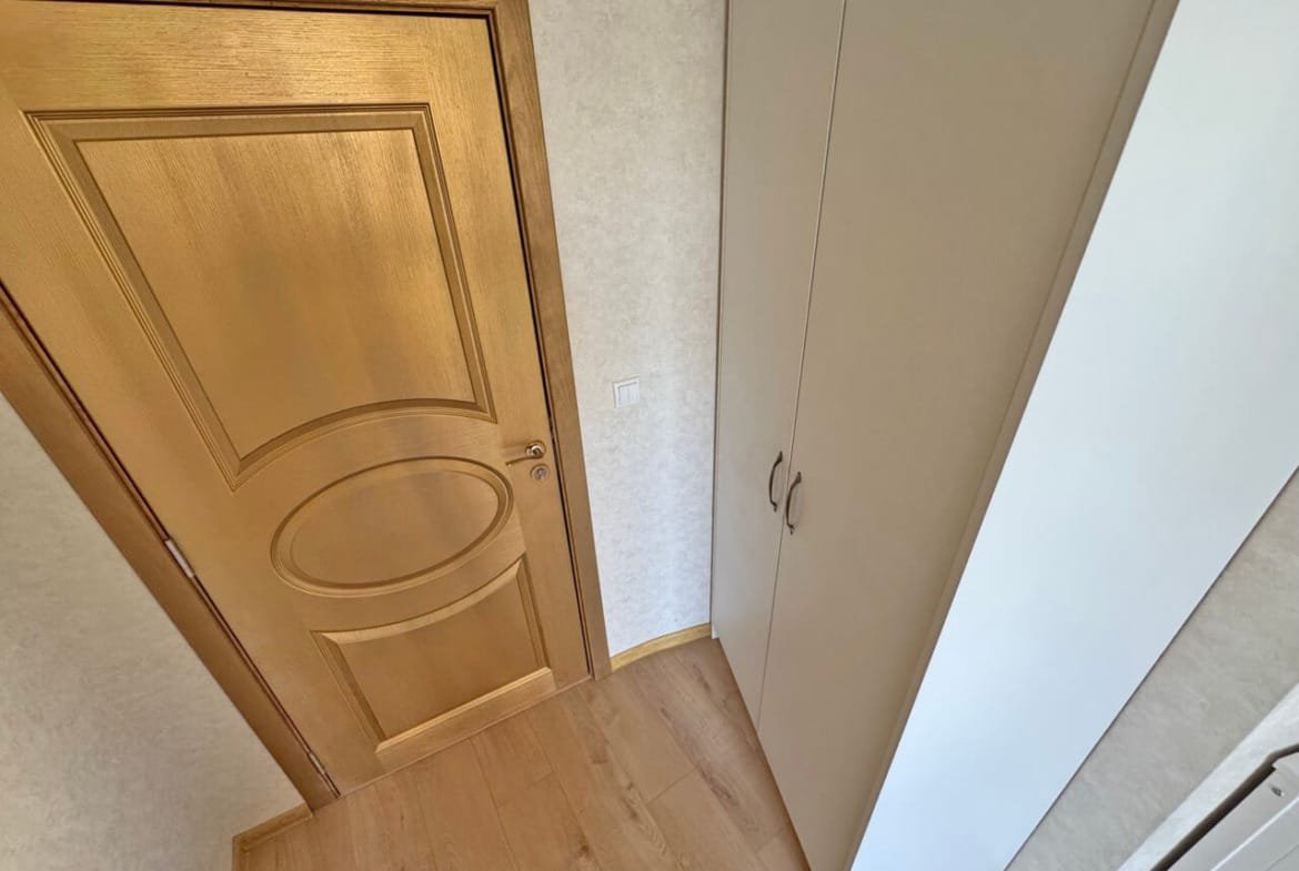 Элегантная входная дверь с золотистой отделкой, рядом шкаф для хранения, теплый пол, светлые тона интерьера.