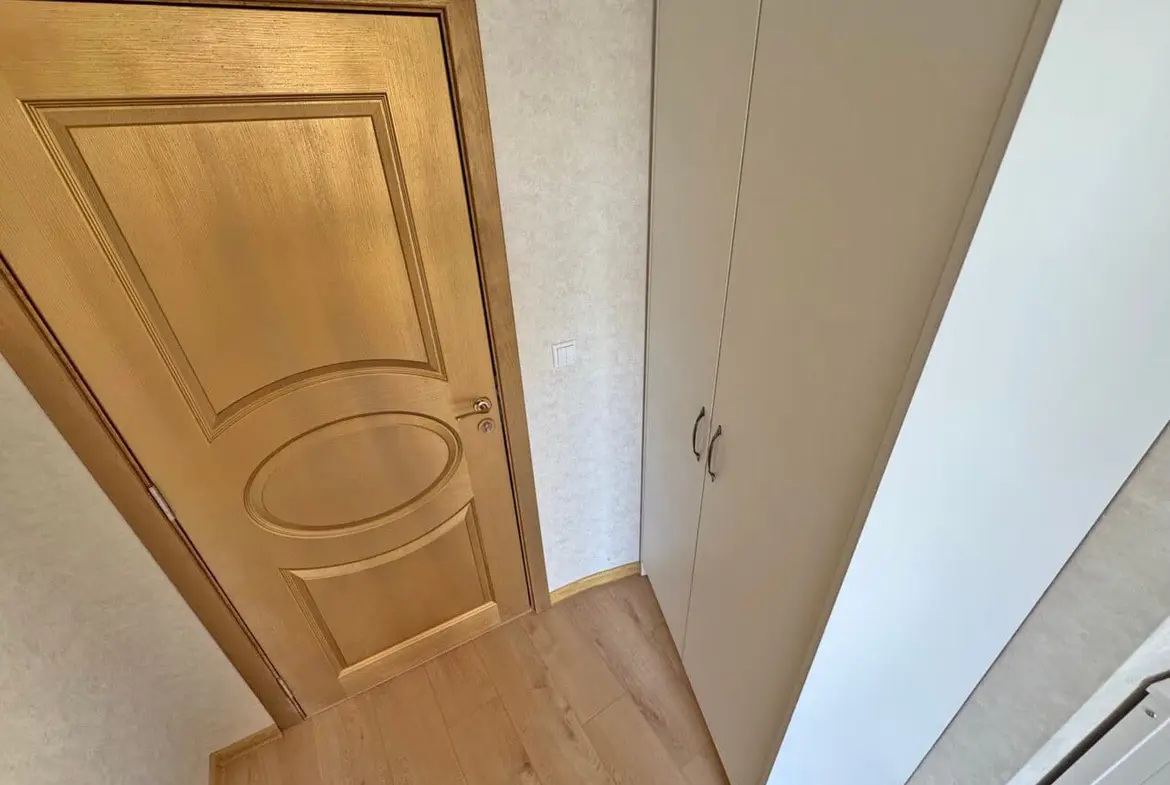 Элегантная входная дверь с золотистой отделкой, рядом шкаф для хранения, теплый пол, светлые тона интерьера.