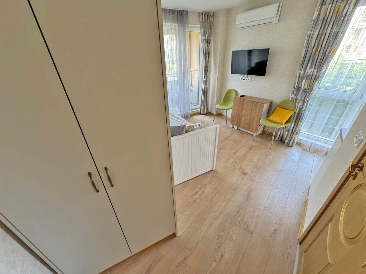 Современный интерьер комнаты с балконом и телевизором Современная гостиная с телевизором и балконом, светлая отделка, удобная мебель, квартира в Болгарии, идеальна для отдыха у моря.