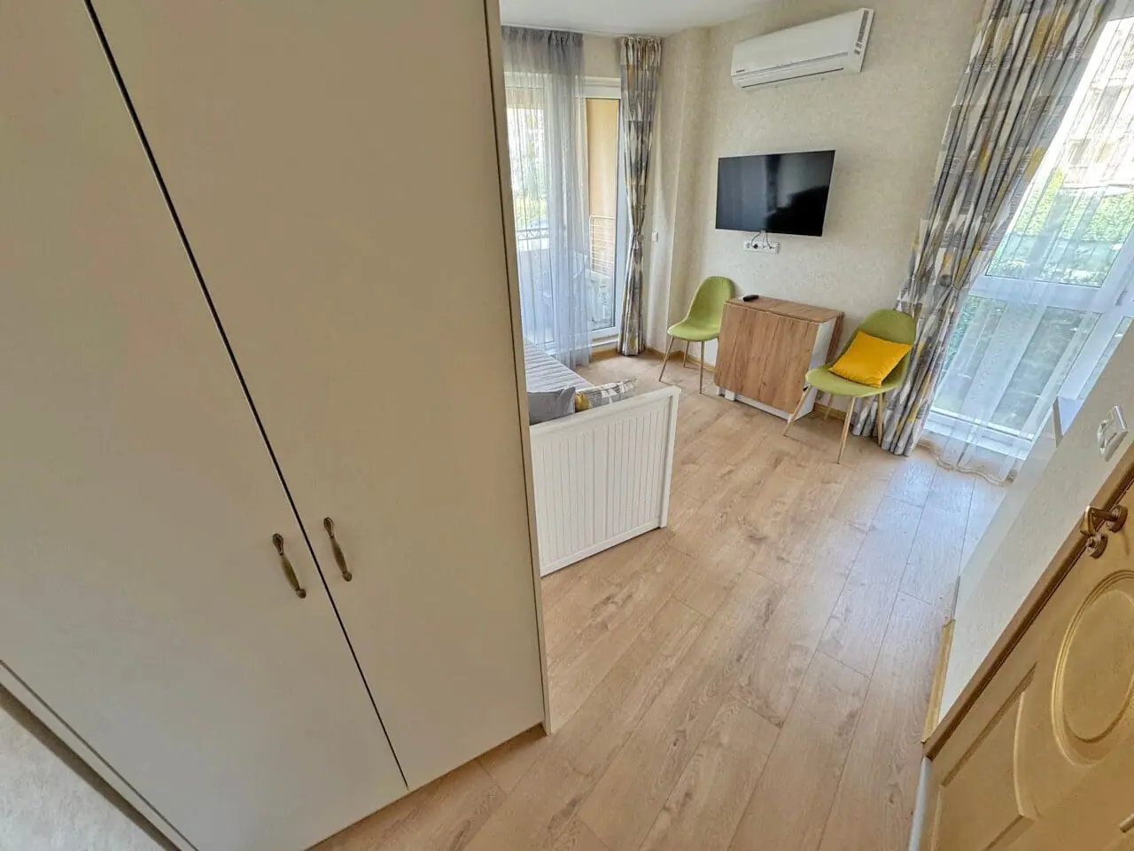 Современный интерьер комнаты с балконом и телевизором Современная гостиная с телевизором и балконом, светлая отделка, удобная мебель, квартира в Болгарии, идеальна для отдыха у моря.