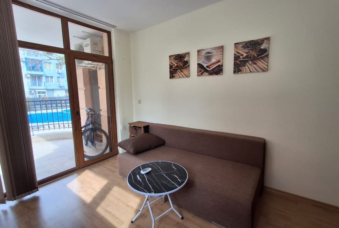 Уютная гостиная с диваном, круглым столиком и окнами, выходящими на балкон с видом на бассейн.