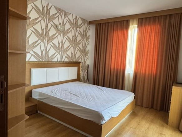 Современная спальня с деревянным полом, светлыми стенами и гардеробом, идеальная для покупки недвижимости в Болгарии.