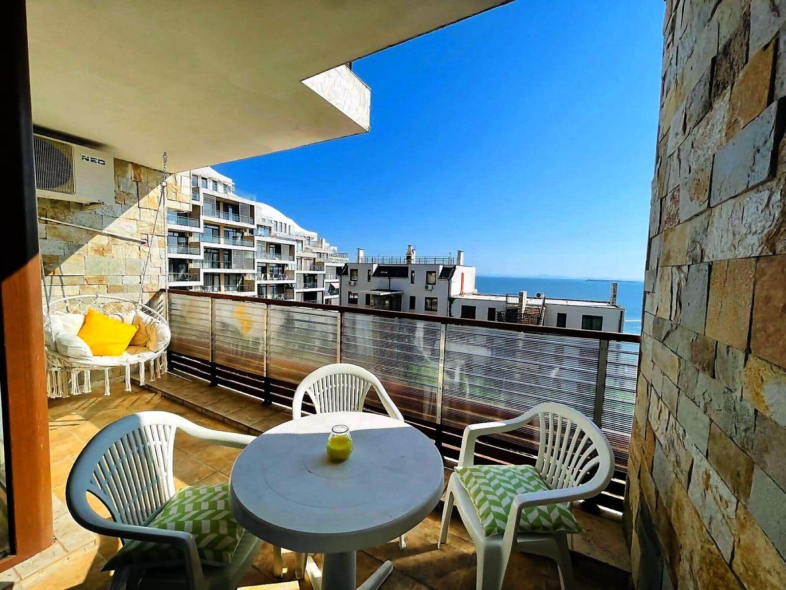 Балкон с белыми креслами и круглым столом, вид на море и жилые комплексы в Болгарии, идеальное место для отдыха.