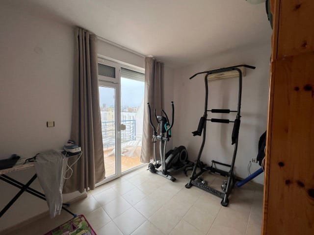 Уютная комната с тренажерами, балконом и светлыми шторами, идеальная для покупки недвижимости в Болгарии.