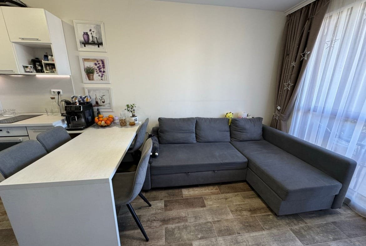 Современная гостиная с серым диваном, обеденным столом, кухонной техникой и яркими декоративными элементами в интерьере.