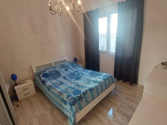 Комфортная спальня с двуспальной кроватью, светлыми тонами, большими окнами и современной мебелью, идеально для покупки недвижимости в Болгарии.