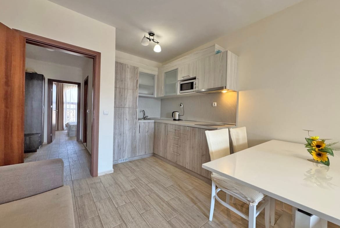 Современная кухня с обеденным столом и стульями, деревянные шкафы и светлые тона. На столе ваза с подсолнухами.