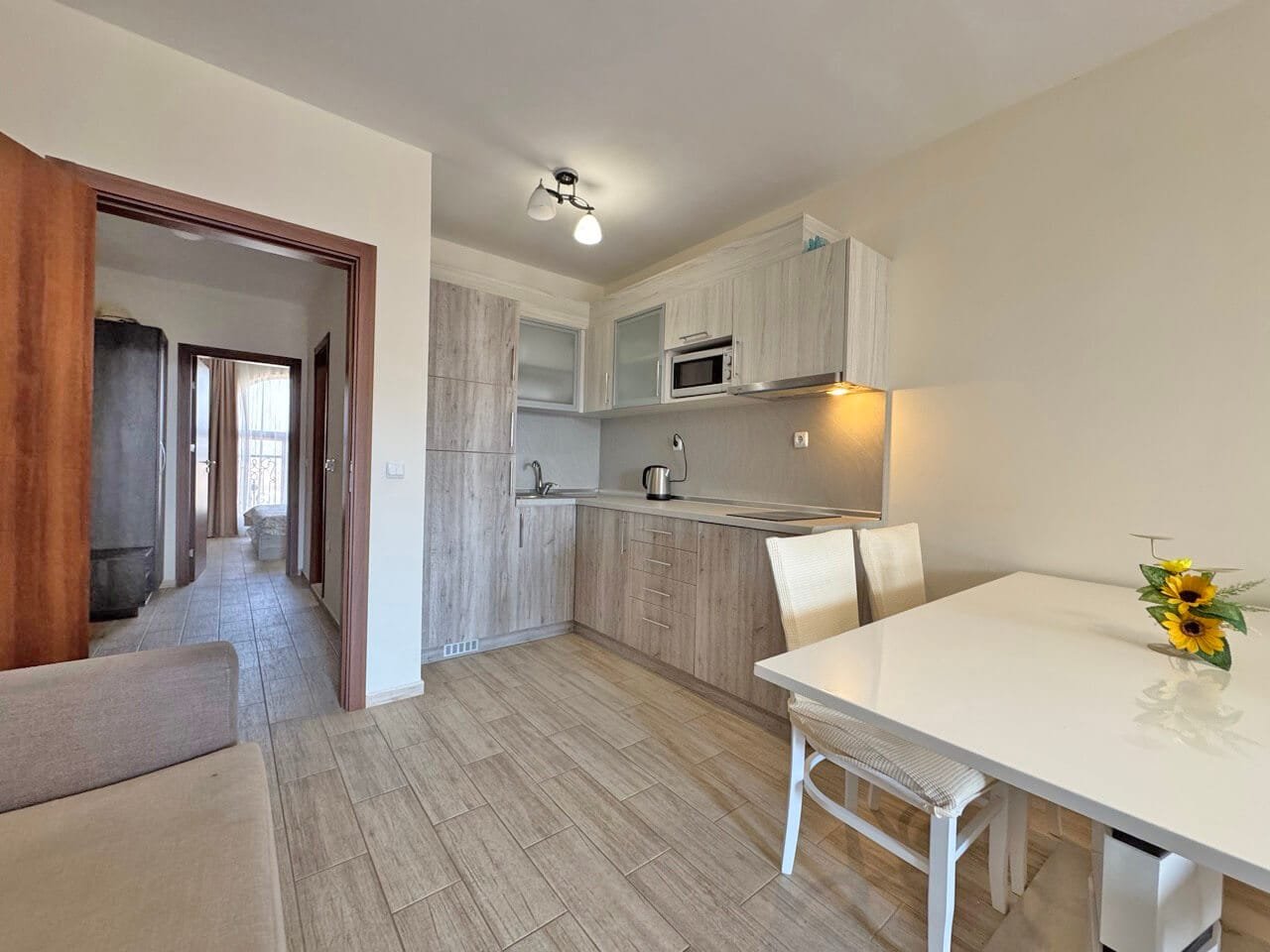 Современная кухня с обеденным столом и стульями, деревянные шкафы и светлые тона. На столе ваза с подсолнухами.