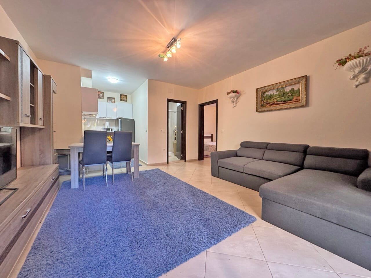 Современная гостиная с серым диваном, столом и стульями, светлым интерьером и синим ковром на полу.