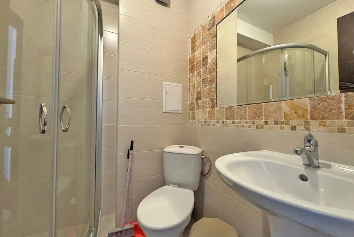 Современная ванная комната с душевой кабиной, унитазом и раковиной, отделанная светлыми плитками и элементами мозаики.