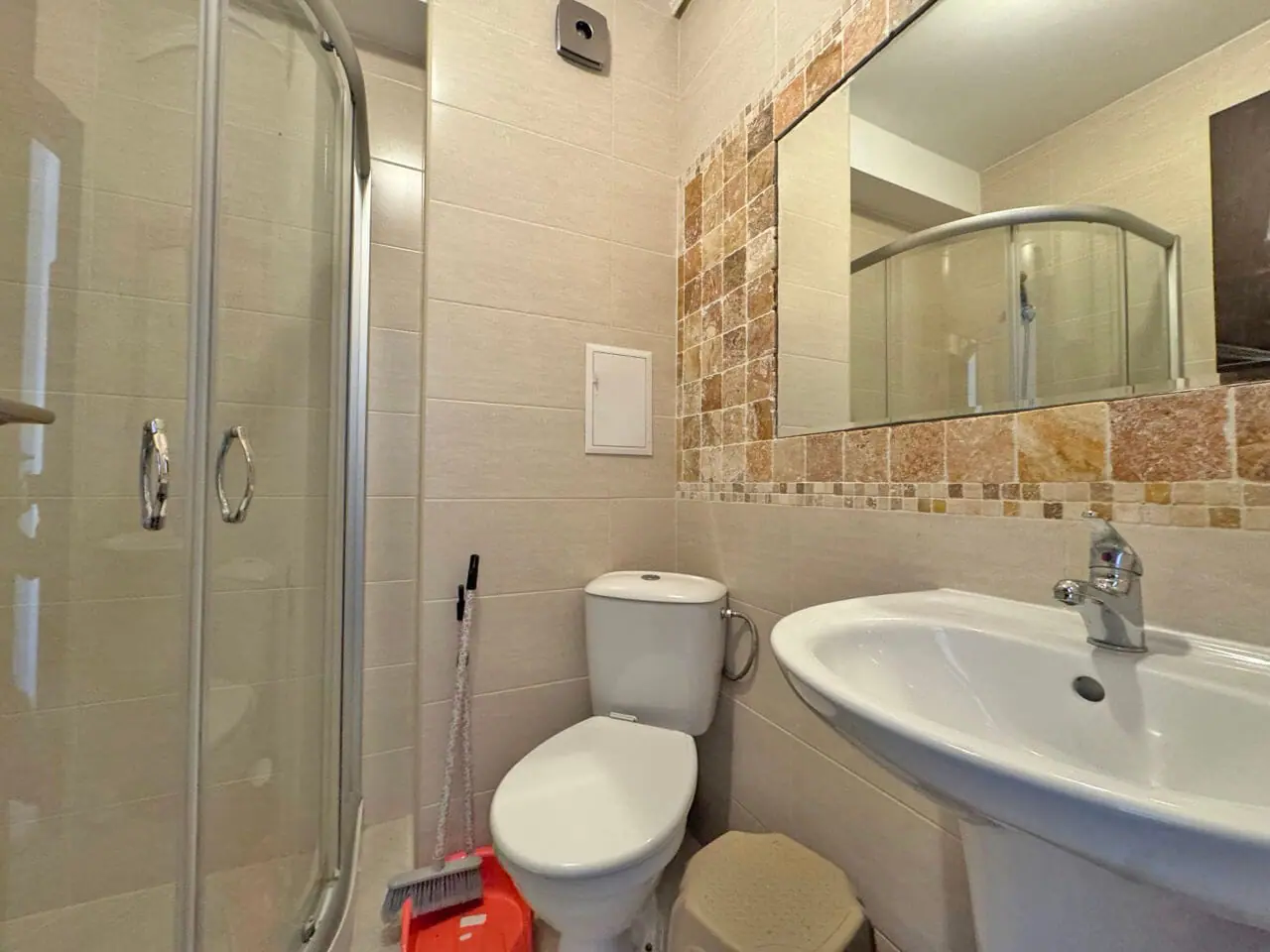 Современная ванная комната с душевой кабиной, унитазом и раковиной, отделанная светлыми плитками и элементами мозаики.