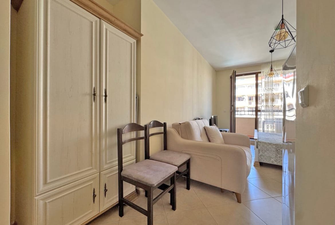 Гостиная с диваном и креслом, шкафом, большим окном и выходом на балкон, удобная для проживания в квартире.