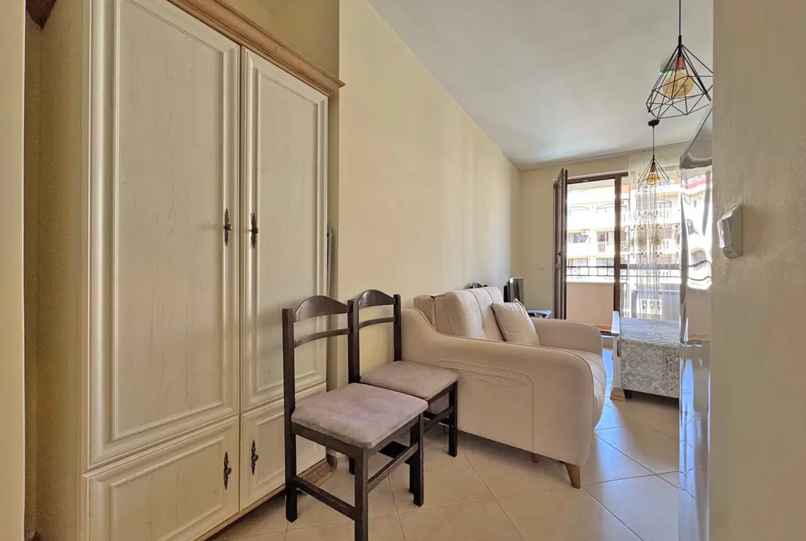 Гостиная с диваном и креслом, шкафом, большим окном и выходом на балкон, удобная для проживания в квартире.