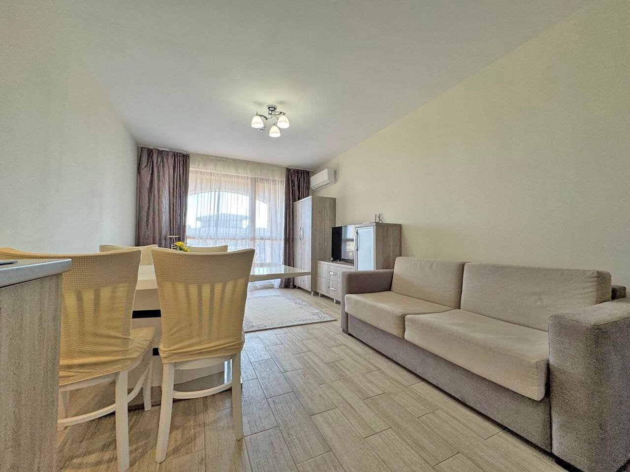 Современный интерьер квартиры с диваном, обеденным столом и светлыми шторами, создающий уютную атмосферу.