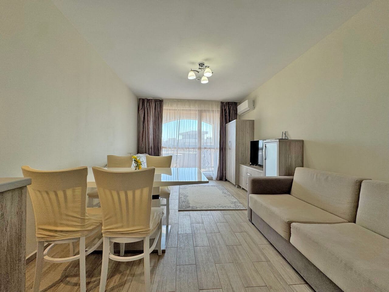 Современный интерьер квартиры с обеденным столом, удобным диваном и телевизором, светлые цвета и окна с видом.