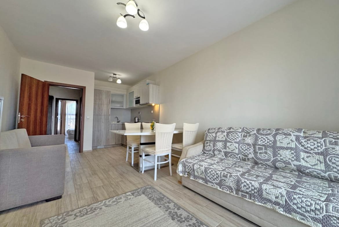 Современный интерьер: светлая гостиная с диваном, столом и стульями, деревянный пол, кухня в домике.