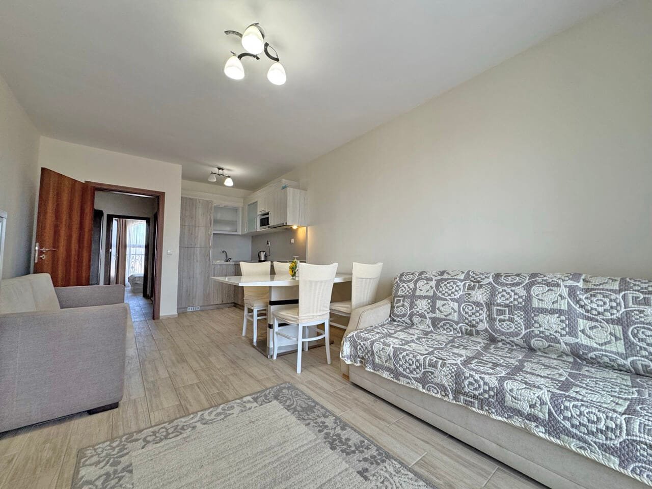 Современный интерьер: светлая гостиная с диваном, столом и стульями, деревянный пол, кухня в домике.