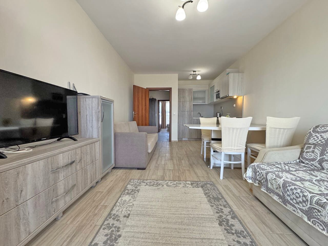 Современный интерьер квартиры с серым диваном, телевизором, столом и стульями, светлыми тонами и уютной атмосферой.