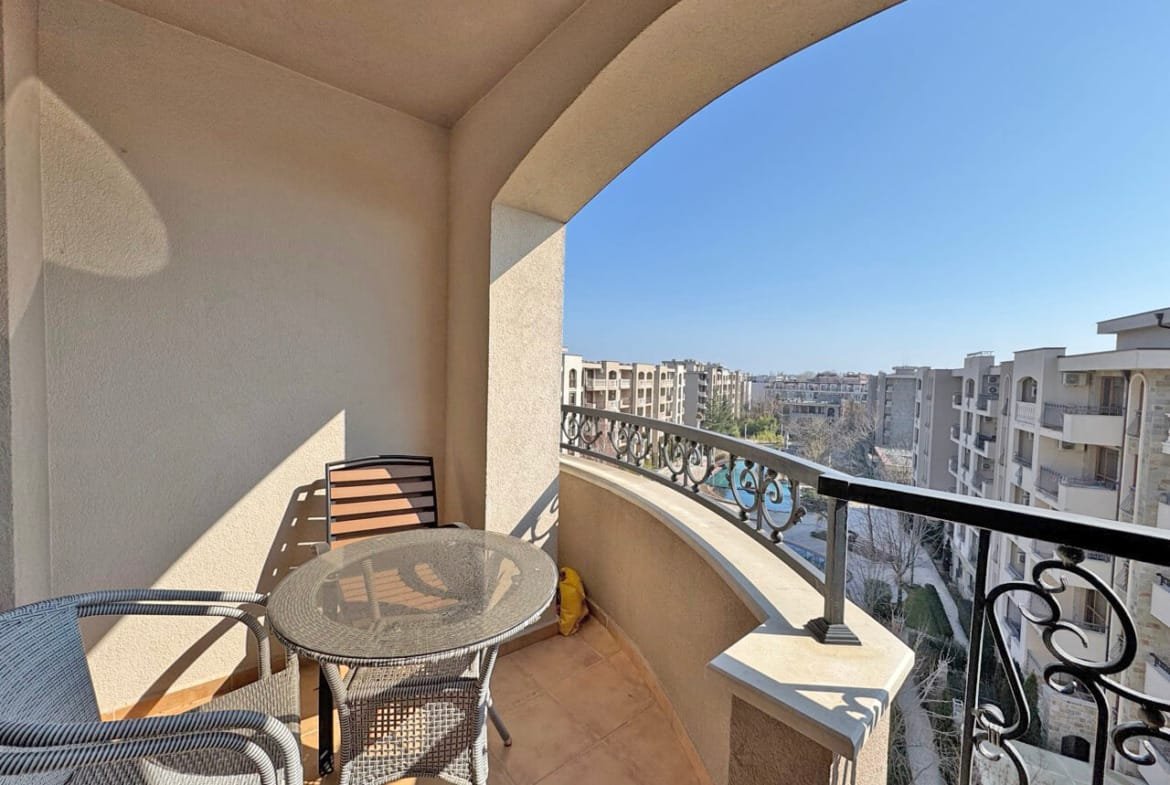 Балкон с круглым столом и стульями, overlooking жилые здания и ясное голубое небо.