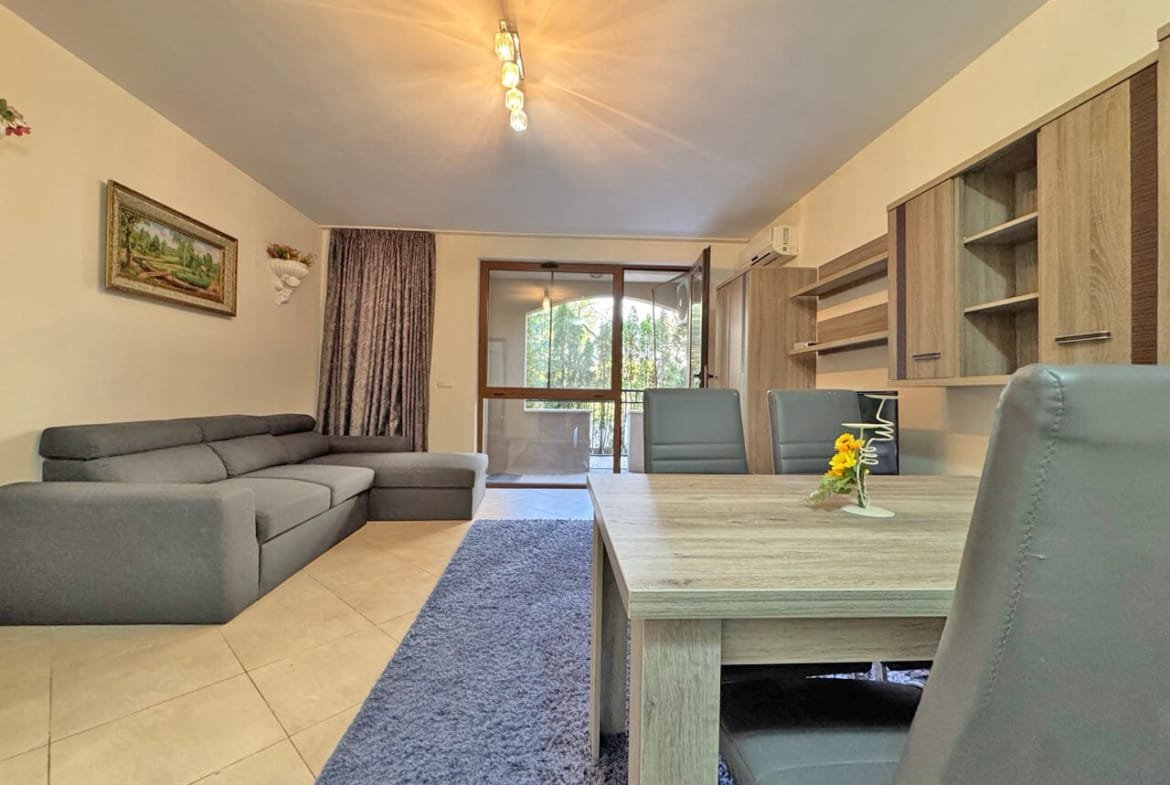 Современный интерьер квартиры с серым диваном, деревянным столом и окнами, обеспечивающими естественное освещение.