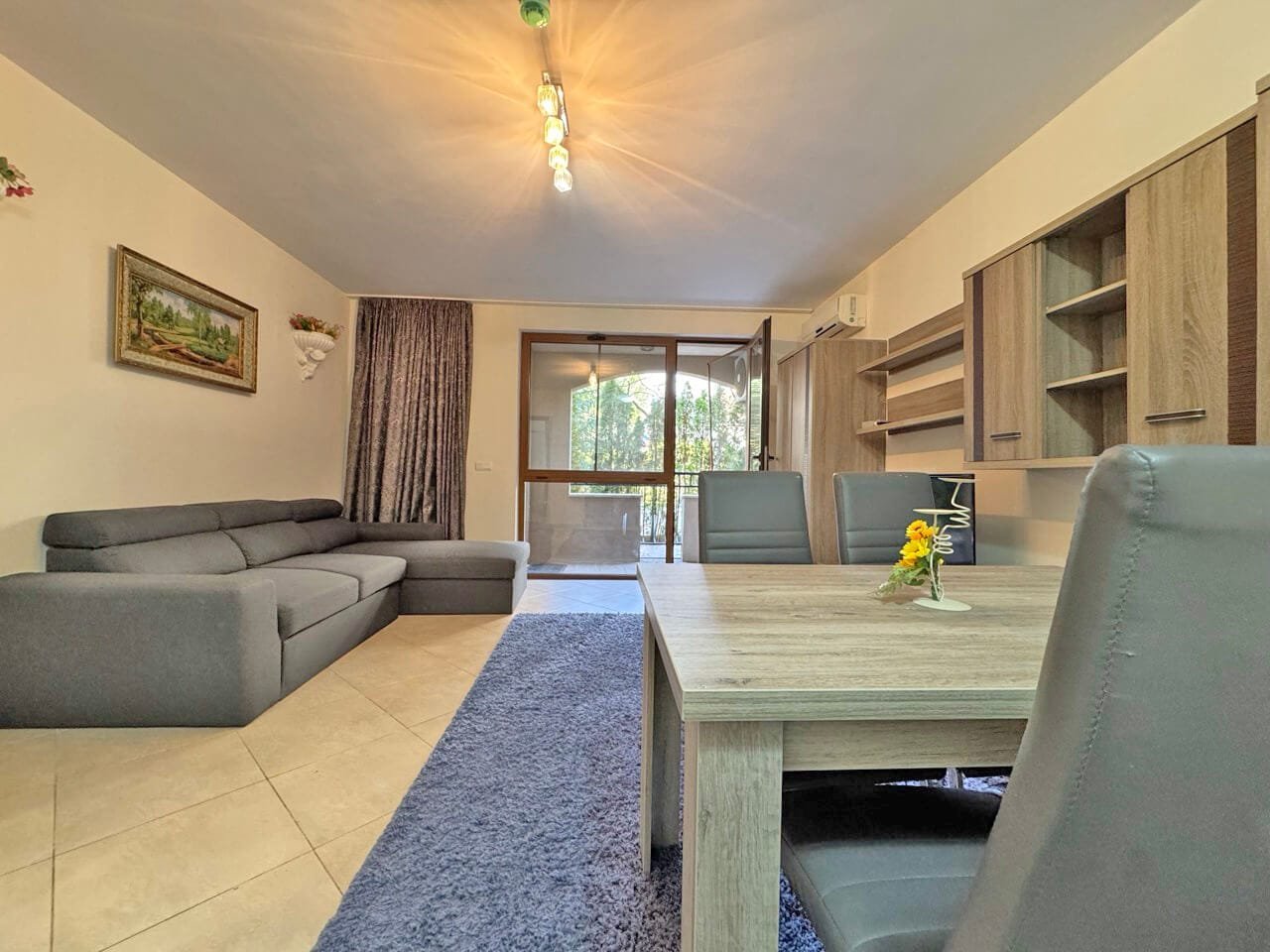 Современный интерьер квартиры с серым диваном, деревянным столом и окнами, обеспечивающими естественное освещение.