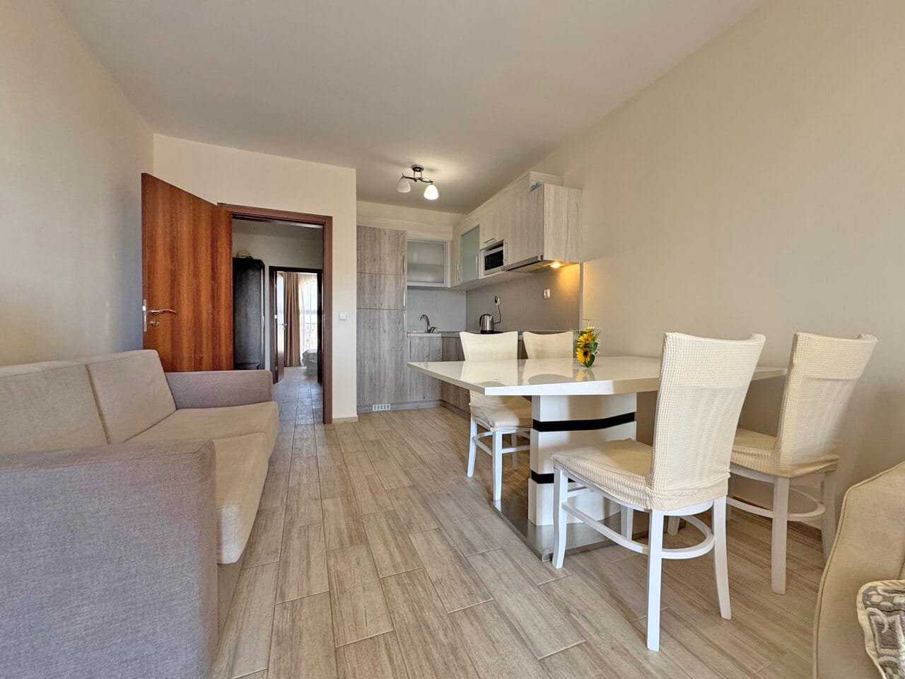 Современная светлая гостиная с кухней, обеденным столом и стульями, уютным диваном и натуральными оттенками отделки.