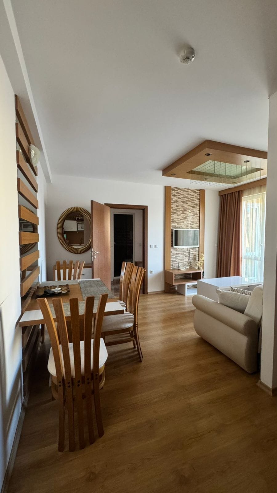 Современная гостиная с кухонным столом, деревянными стульями и мягкой мебелью в квартире в Болгарии, идеальной для продажи или аренды.