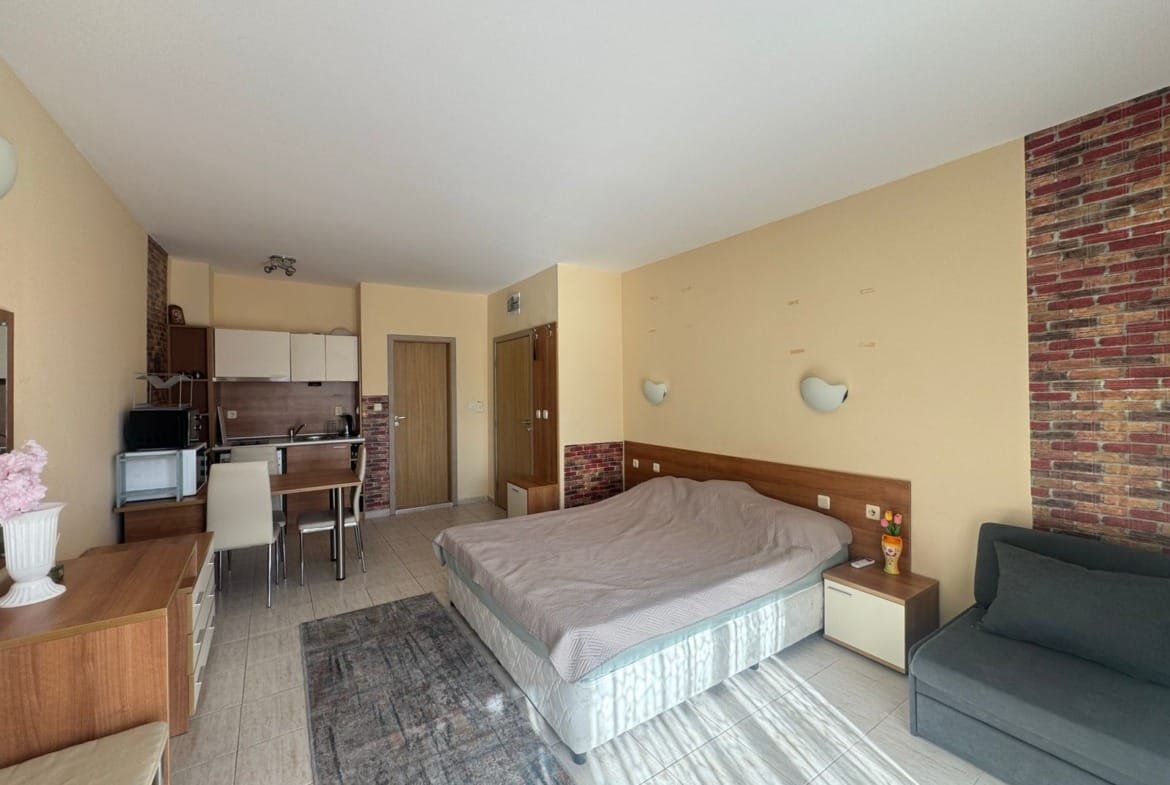 Уютная студия с двуспальной кроватью, кухонной зоной и теплыми тонами в интерьере, идеально подходит для покупки в Болгарии.