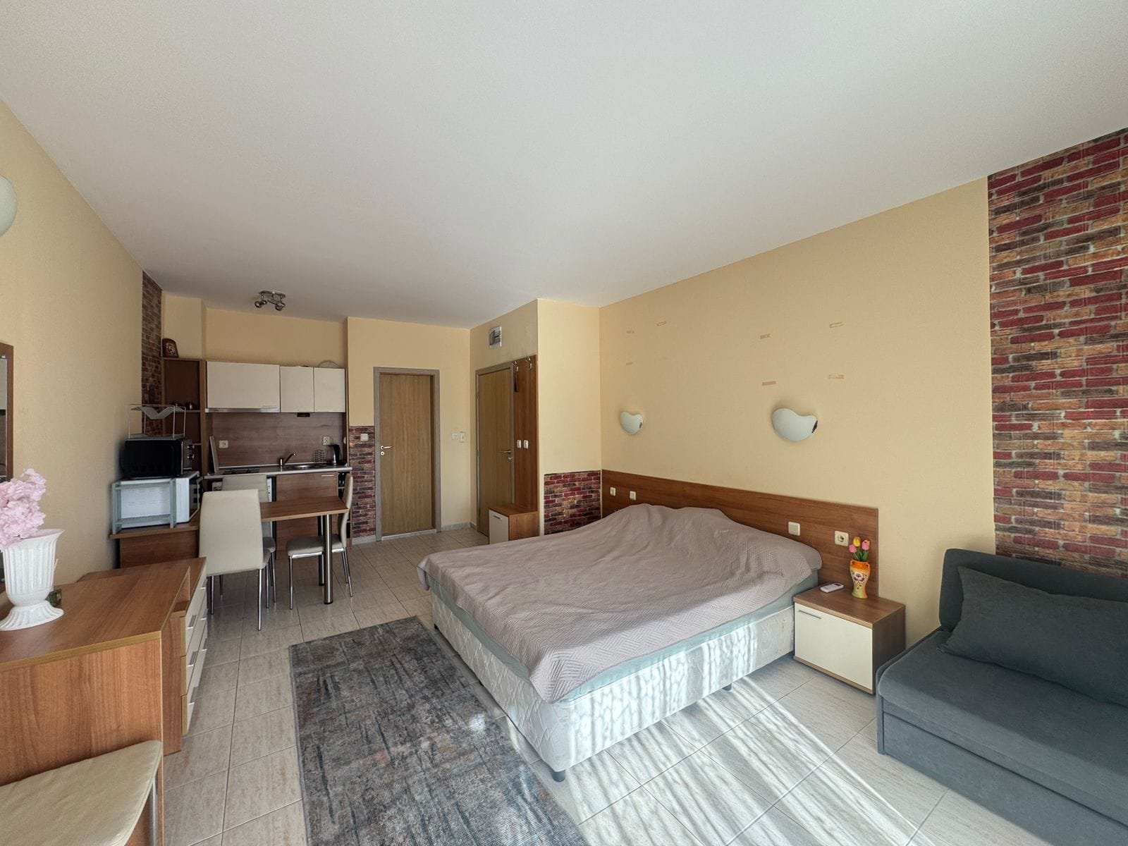 Уютная студия с двуспальной кроватью, кухонной зоной и теплыми тонами в интерьере, идеально подходит для покупки в Болгарии.