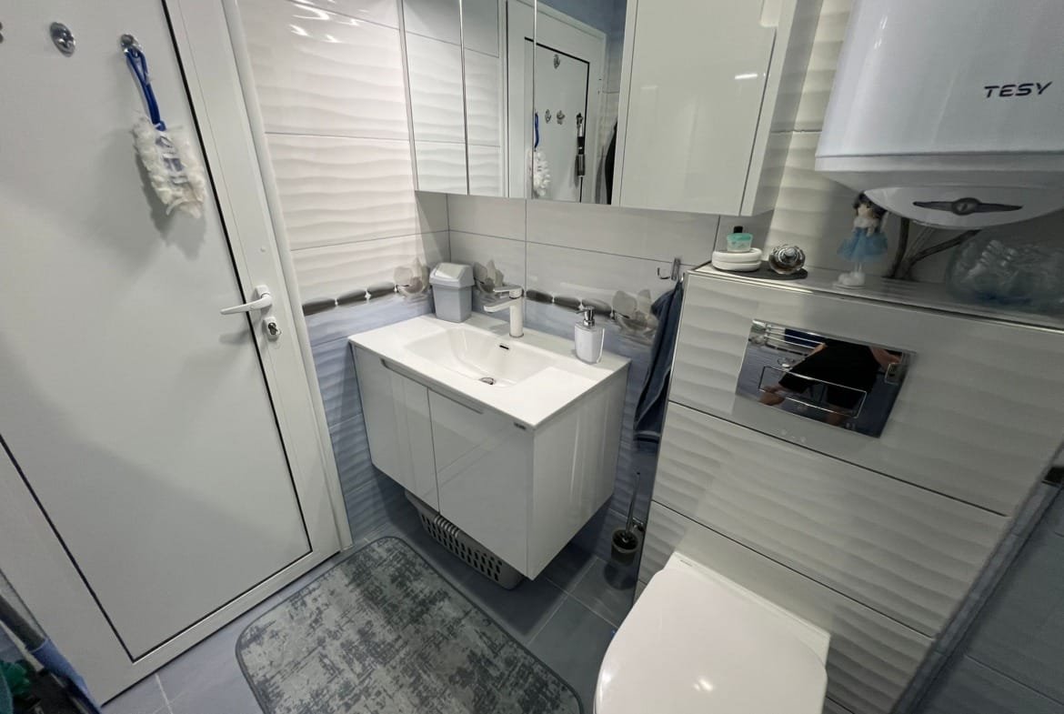 Современный интерьер ванной комнаты с белой сантехникой, стеклянными полками и светлыми стенами в Болгарии.