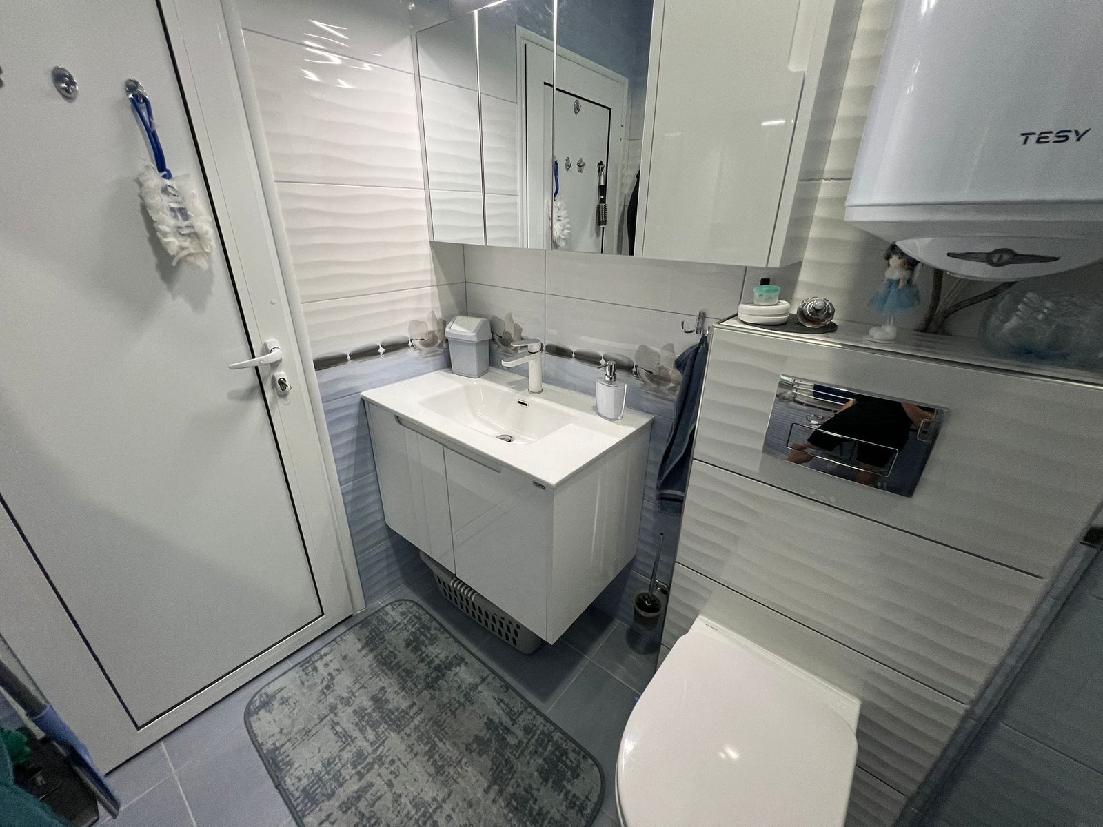 Современный интерьер ванной комнаты с белой сантехникой, стеклянными полками и светлыми стенами в Болгарии.