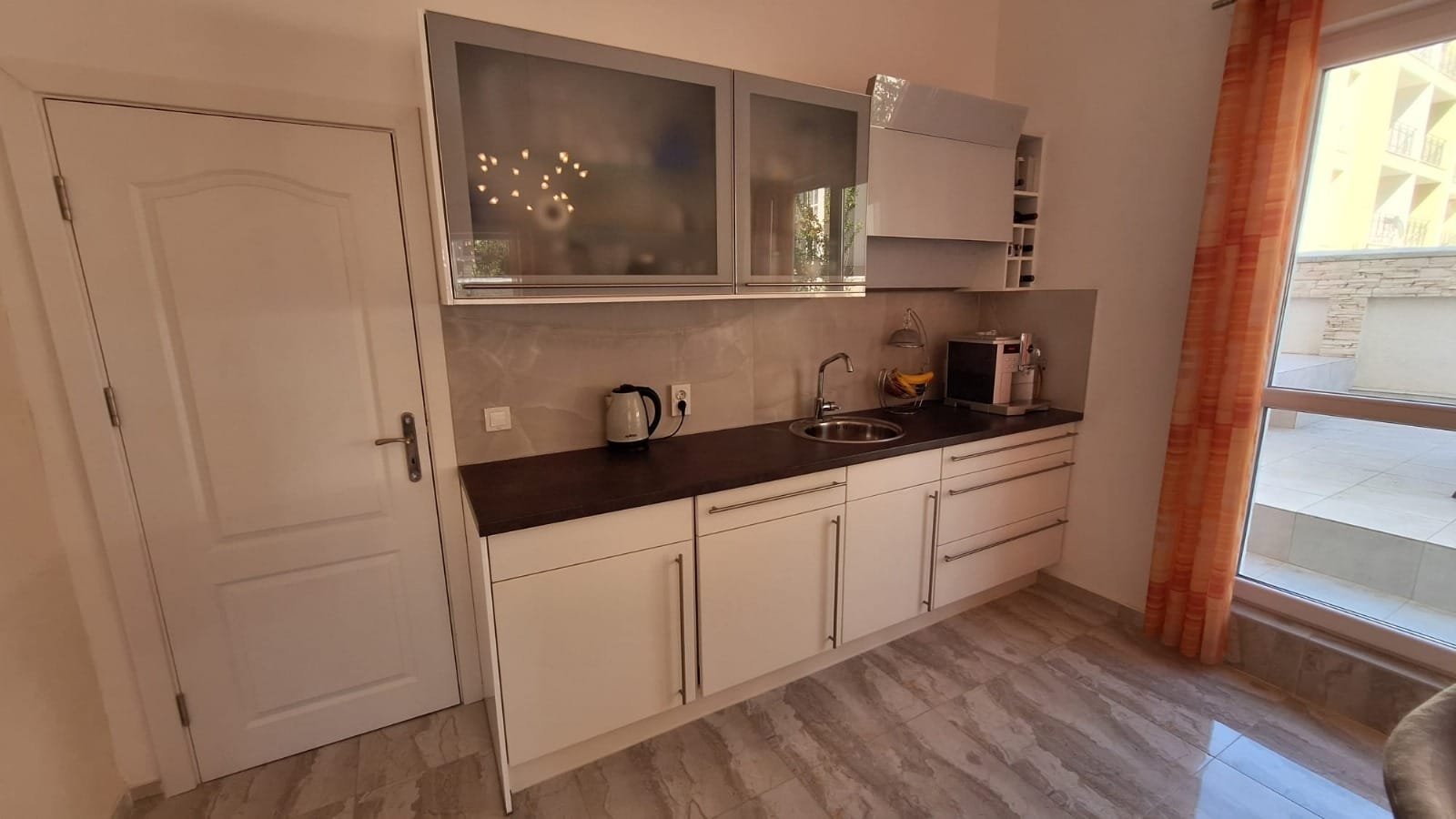 Современная кухня с белыми шкафами, черной столешницей и техническими приборами, идеально подходит для покупки недвижимости в Болгарии.