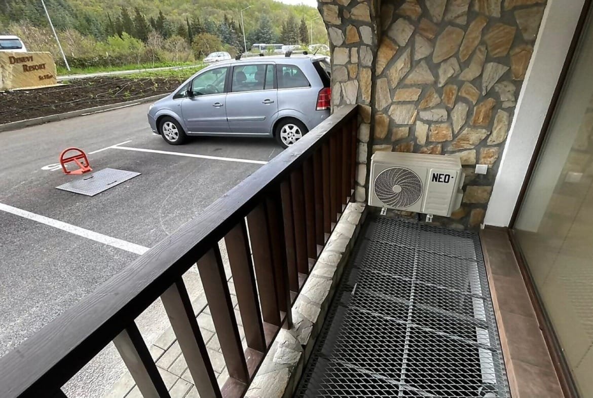 Балкон с решетчатым полом, кондиционером и видом на парковку с автомобилями, подходит для отдыха в Болгарии.